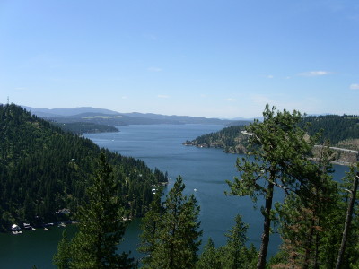 [Looking down on the lake below from a nearby mountain ridge. The lake has a zig-zag shape and the shores are varying slopes of evergreen-covered hills.]